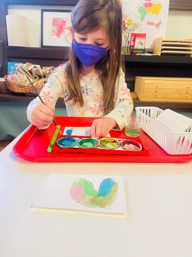 Child concentrating on watercolor painting, developing artistic skills and creative expression in Montessori art program